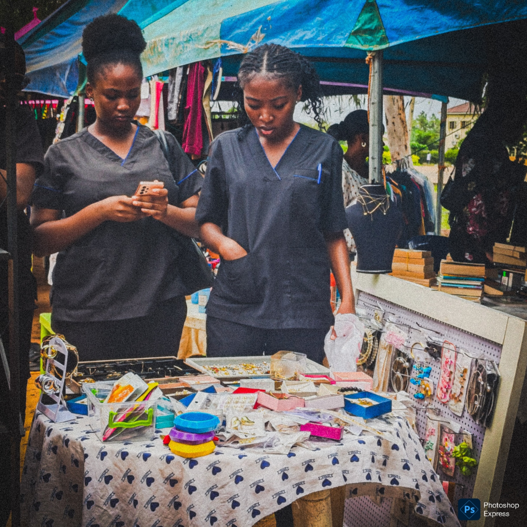 Two women browsing a market stall with jewelry and accessories on display.